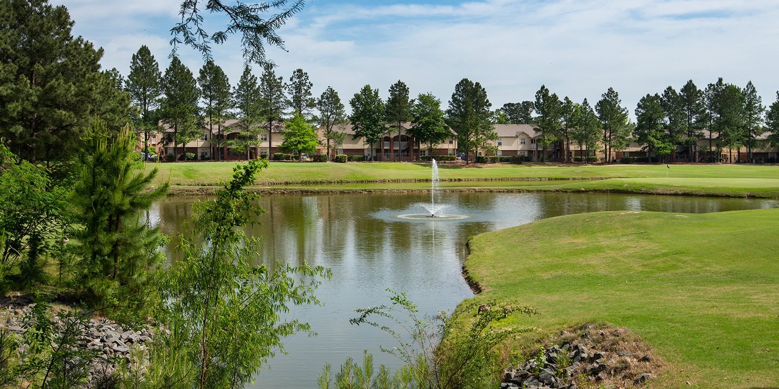 A golf course with a pond and a fountain in the middle.
